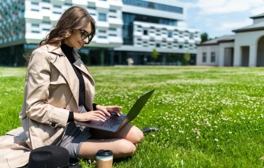 Estudiante trabajando con su laptop en un espacio verde del campus